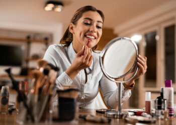 Young smiling woman applying lip liner while looking herself in