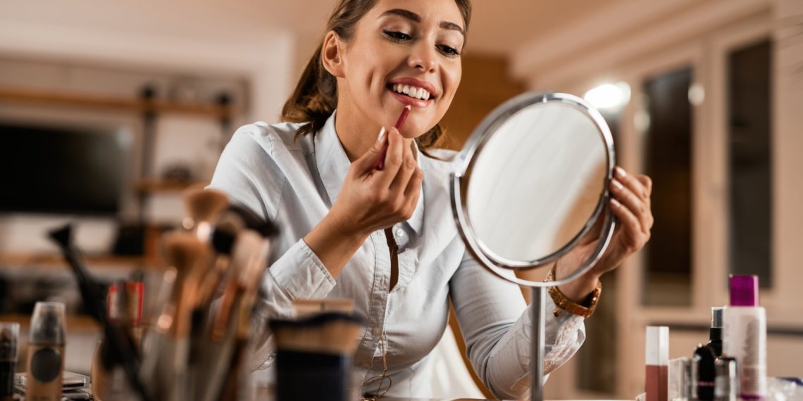 Young smiling woman applying lip liner while looking herself in